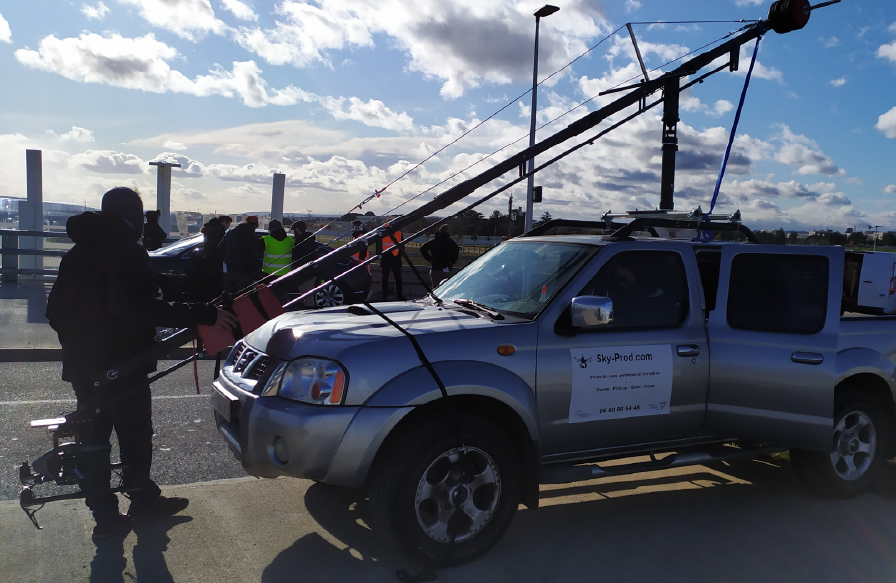 Pick-up de tournage avec doubles plateformes et bazookas pour grue : manipulation sécurisée par harnais et contrôle en cabine.