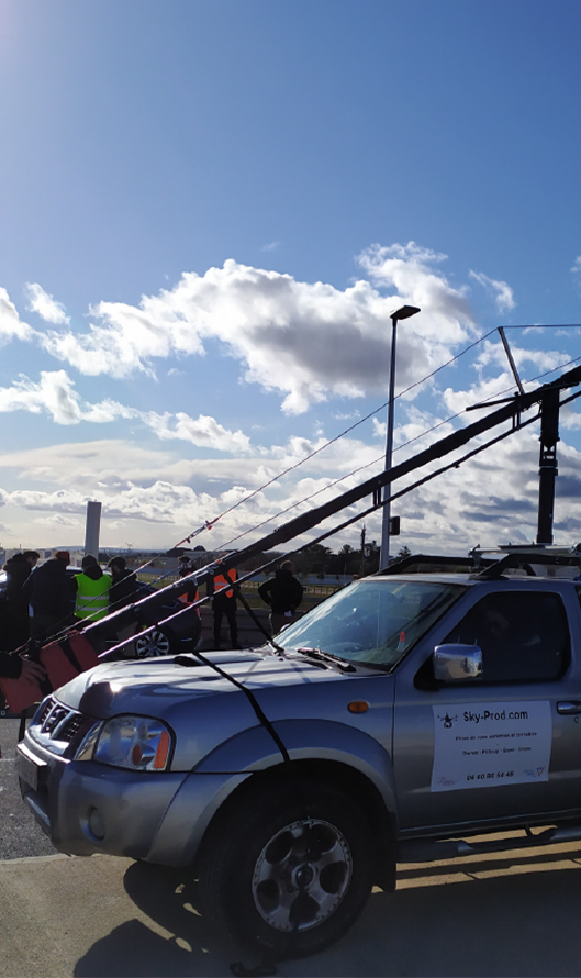 Pick-up de tournage avec doubles plateformes et bazookas pour grue : manipulation sécurisée par harnais et contrôle en cabine.