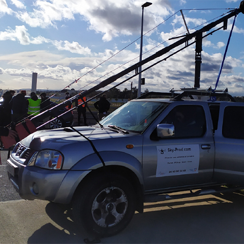 Pick-up de tournage avec doubles plateformes et bazookas pour grue : manipulation sécurisée par harnais et contrôle en cabine.